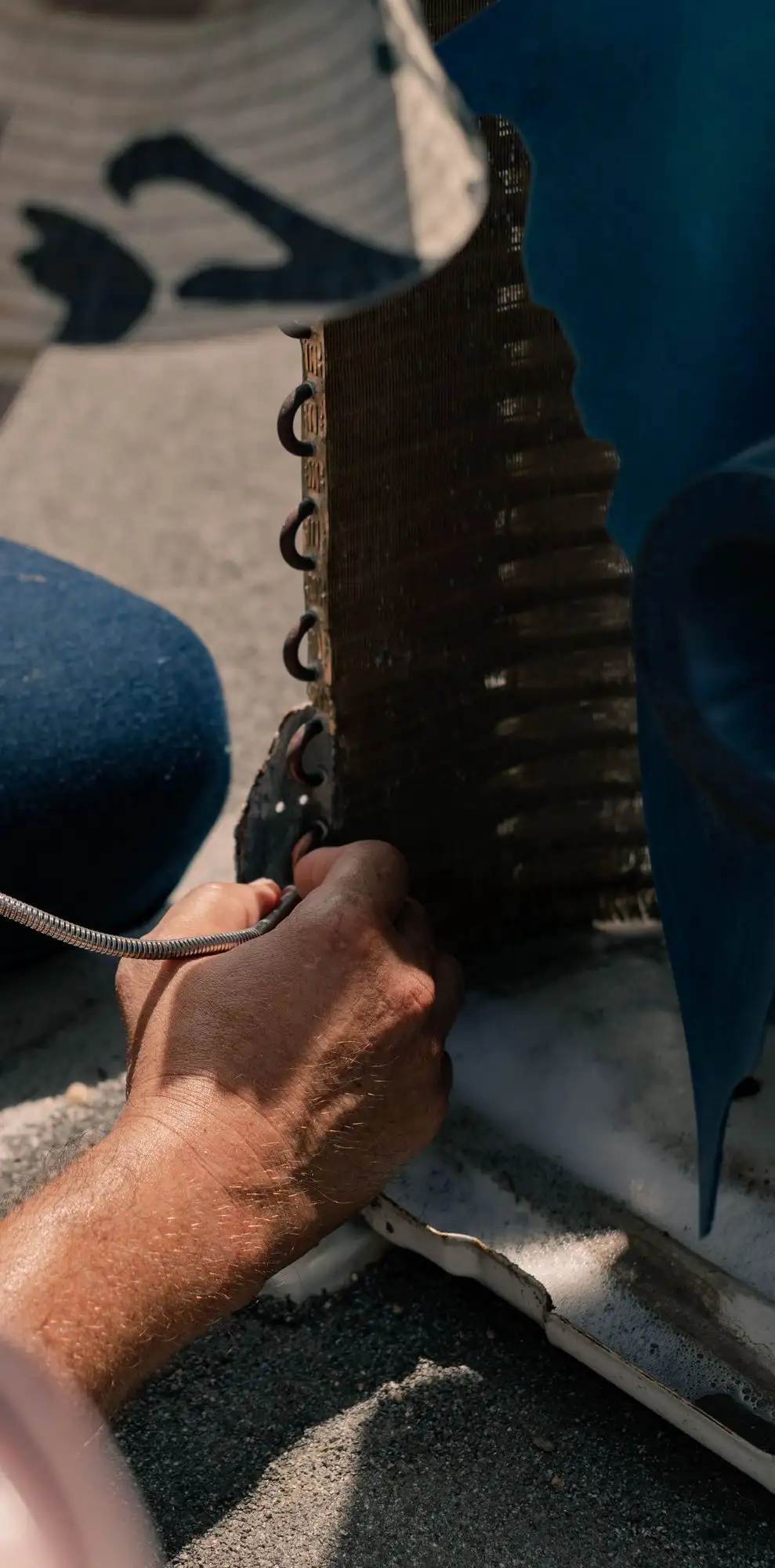 Technician's hand guiding a leak-detector probe along the copper bends of an outdoor unit's coil
