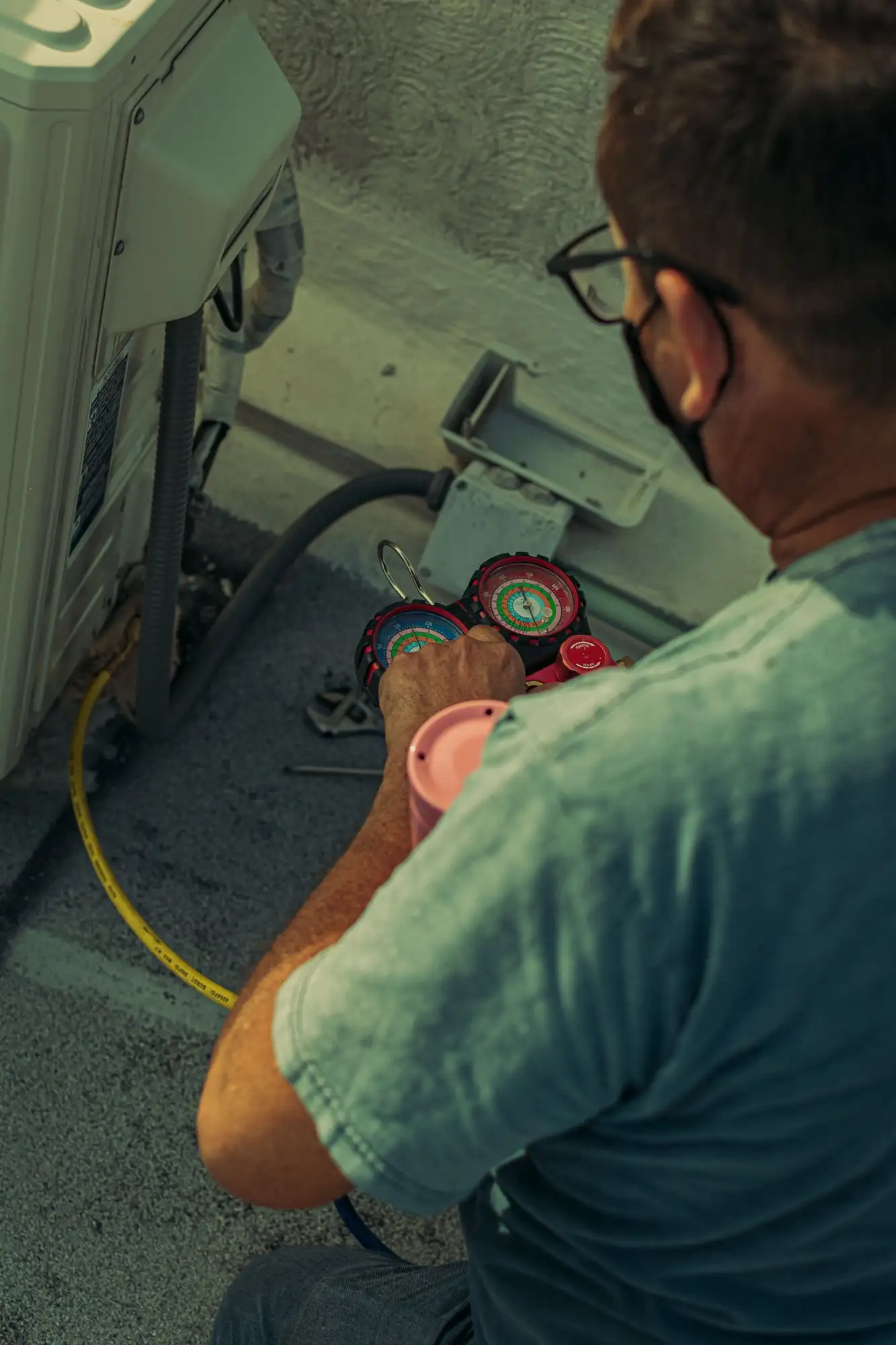 Technician crouched beside an outdoor unit with a refrigerant gauge set in hand