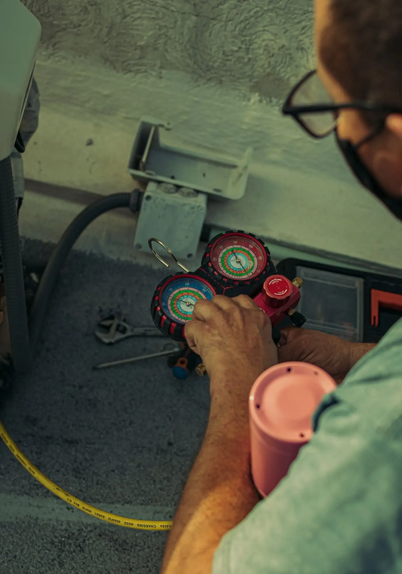 Hands holding a refrigerant manifold gauge set connected to an outdoor unit